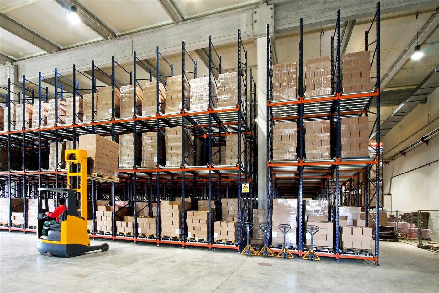 Warehouse pallet racking stacked with boxes, with a forklift operator retrieving stock